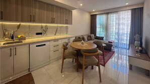 Uma cozinha moderna com painel de parede de mármore, uma sala de jantar com uma mesa redonda e cadeiras, e uma sala de estar com sofá e uma janela grande.