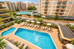 Une piscine sur le toit, agrémentée de chaises longues et de parasols, entourée d’immeubles de grande hauteur et de verdure.