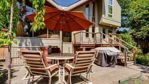 Une terrasse avec une table et des chaises, un barbecue couvert et un escalier menant à une plateforme.