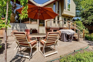 A patio with a table and chairs, a covered grill, and a staircase leading to a deck. - 2BR + Loft Space | 5 Min to Autzen & River (Springfield)