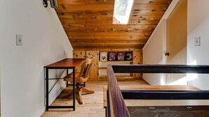 Une chambre à coucher aménagée dans un espace sous les toits, avec un plafond en pente, des poutres en bois, un bureau, une chaise et un lit.