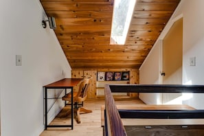 A loft bedroom with a sloped ceiling, wooden beams, a desk, a chair, and a bed. - 2BR + Loft Space | 5 Min to Autzen & River (Springfield)