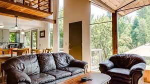 Un vaste espace de vie doté d’un plafond haut, de poutres apparentes, d’un canapé en cuir, d’une table basse en bois et d’une grande fenêtre offrant une vue sur l’extérieur.