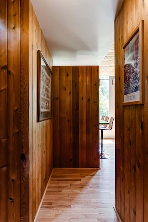 Un couloir en bois, avec un tableau encadré sur le mur à gauche et une chaise au fond.