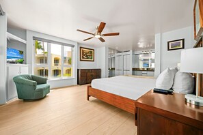 A hotel room with a bed, a green armchair, a ceiling fan, a large window with a view, and a bathroom with a mirror and sink. - Palms at Wailea Villa 404 Garden Deluxe 2 BD 2 BA (Wailea)