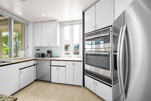 A modern kitchen with white cabinetry, a stainless steel refrigerator, and a double oven. - Palms at Wailea Villa 404 Garden Deluxe 2 BD 2 BA (Wailea)
