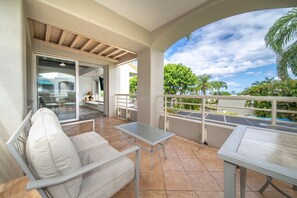 Ein Balkon mit einer weißen Couch, einem kleinen Tisch und einer Glastür zu einem Innenbereich mit einem Sessel und einer Lampe.