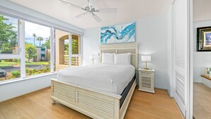 Une chambre à coucher avec un lit, un ventilateur de plafond, une table de chevet avec une lampe et un tableau au mur.