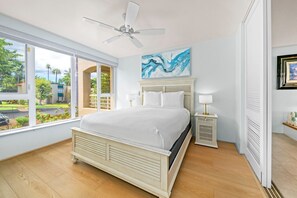 Ein Schlafzimmer mit einem Bett, einem Deckenventilator, einem Nachttisch mit Lampe und einem Gemälde an der Wand.