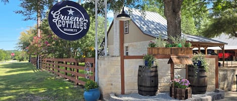 A sign for Gruene Cottages with a rustic stone building, wooden barrels, and potted plants.