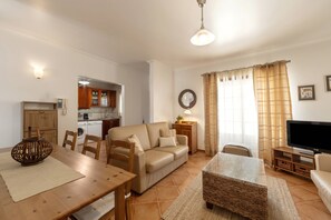 A living room with a sofa, TV, and a dining area with a table and chairs. - Casa Burgues Mar & Lagoa - Private Pool (Óbidos)