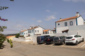 A row of white houses with blue trim and orange roofs, parked cars, and a clear sky. - Casa Burgues Mar & Lagoa - Private Pool (Óbidos)