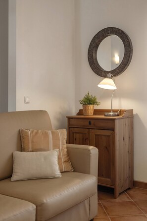 A living room with a sofa, a wooden side table, a lamp, and a mirror. - Casa Burgues Mar & Lagoa - Private Pool (Óbidos)