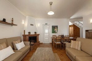 A living room with a fireplace, a dining area, and a staircase leading to an upper floor. - Casa Burgues Mar & Lagoa - Private Pool (Óbidos)