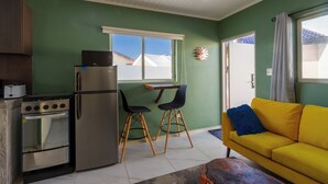 A compact living space with a kitchenette, a dining area with two chairs, a sofa, and a window with a view. - Aruba Vibe Apartments #5 | A charming place near the beaches and the city center (Oranjestad)