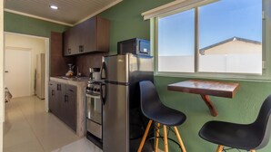 A compact kitchen with a refrigerator, stove, and microwave. There is a small dining area with two chairs and a table. - Aruba Vibe Apartments #5 | A charming place near the beaches and the city center (Oranjestad)