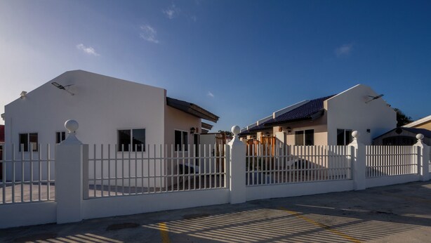 A gated residential area with two houses, a clear sky, and shadows on the ground. - Aruba Vibe Apartments #5 | A charming place near the beaches and the city center (Oranjestad)