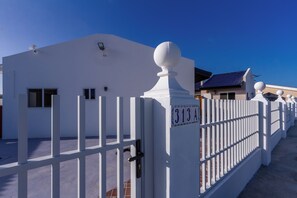 Ein weißes Gebäude mit einer blauen Tür, einem weißen Zaun und wolkenlosem, blauem Himmel.