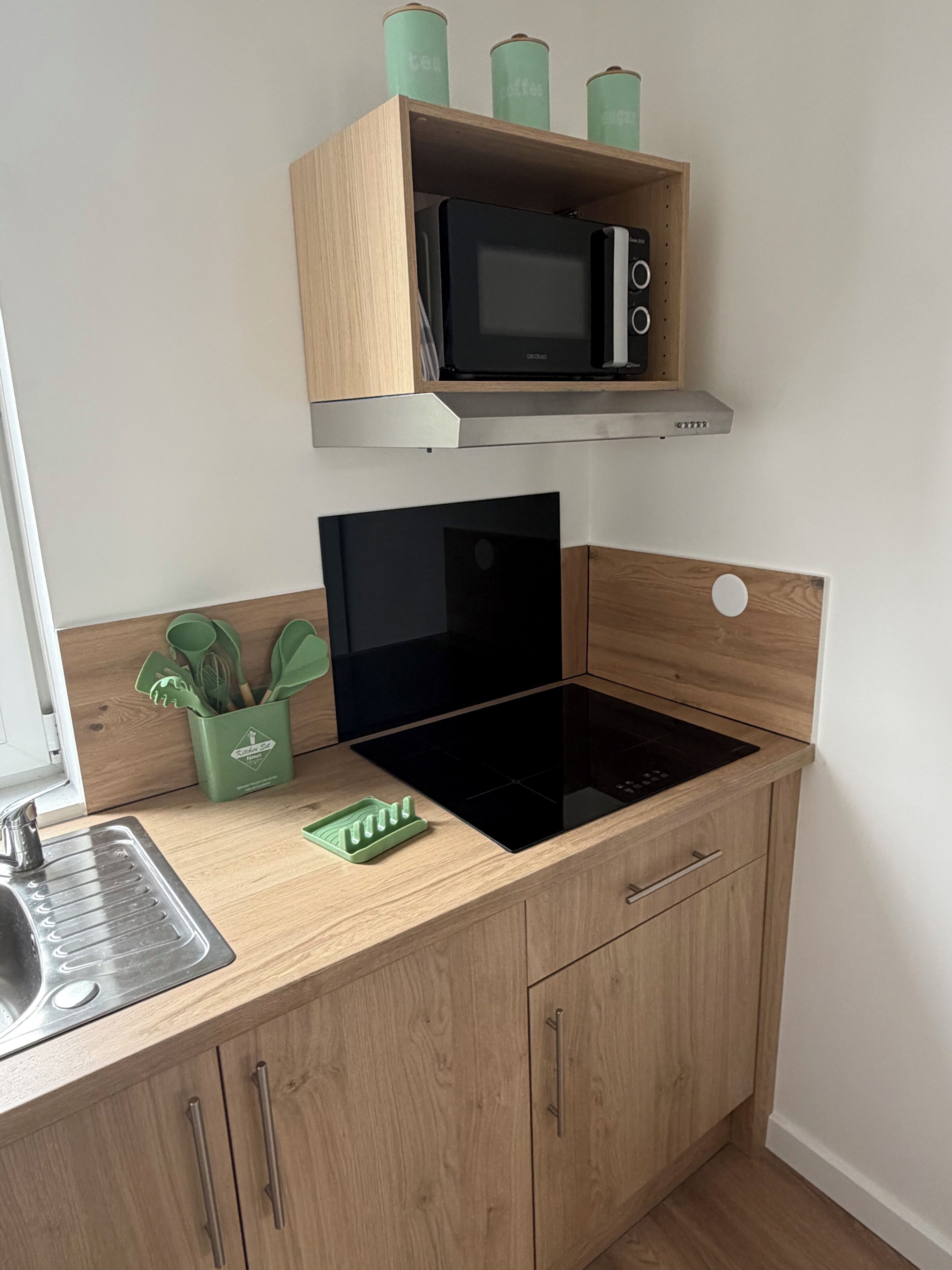 Une cuisine équipée d’un four à micro-ondes, d’une plaque de cuisson à induction noire et de meubles de rangement en bois.