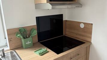 Een keuken met een magnetron, een zwart inductiekookplaat en houten keukenkastjes.