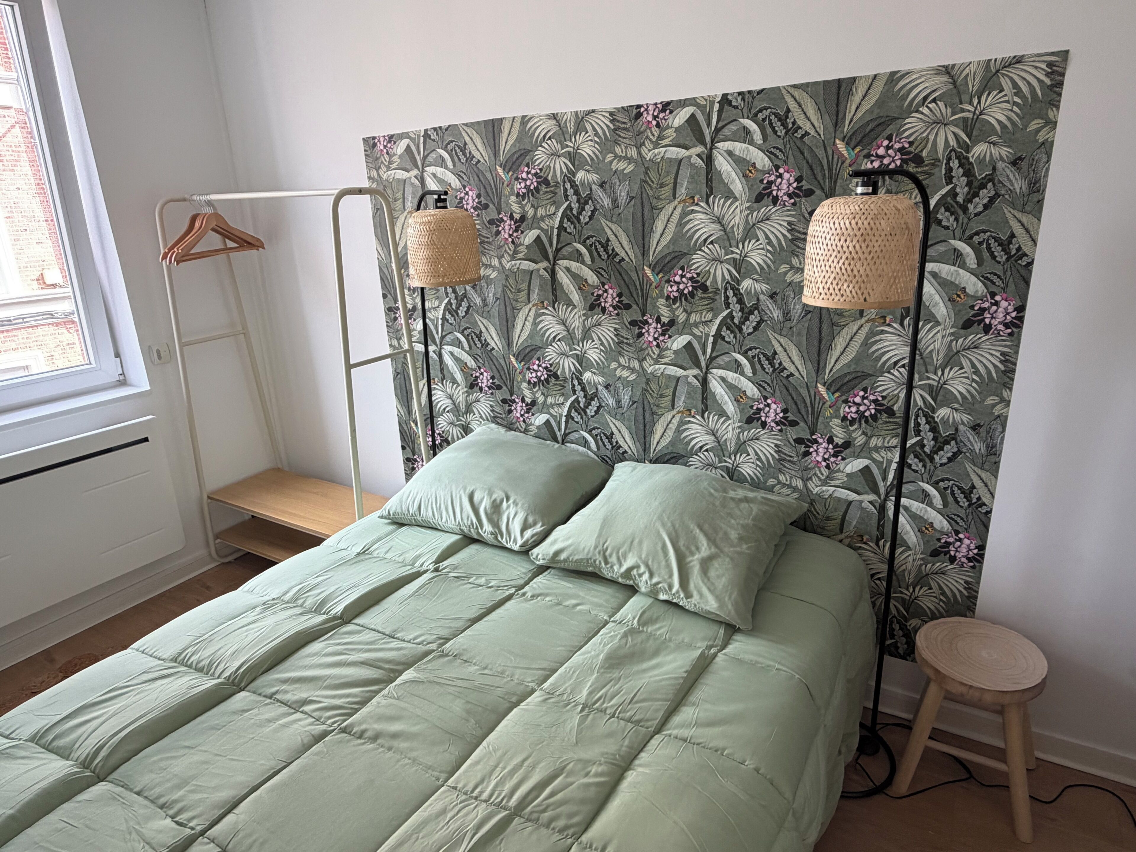Ein Schlafzimmer mit einem Bett, einer Hängelampe, einem hölzernen Hocker und einem Fenster.