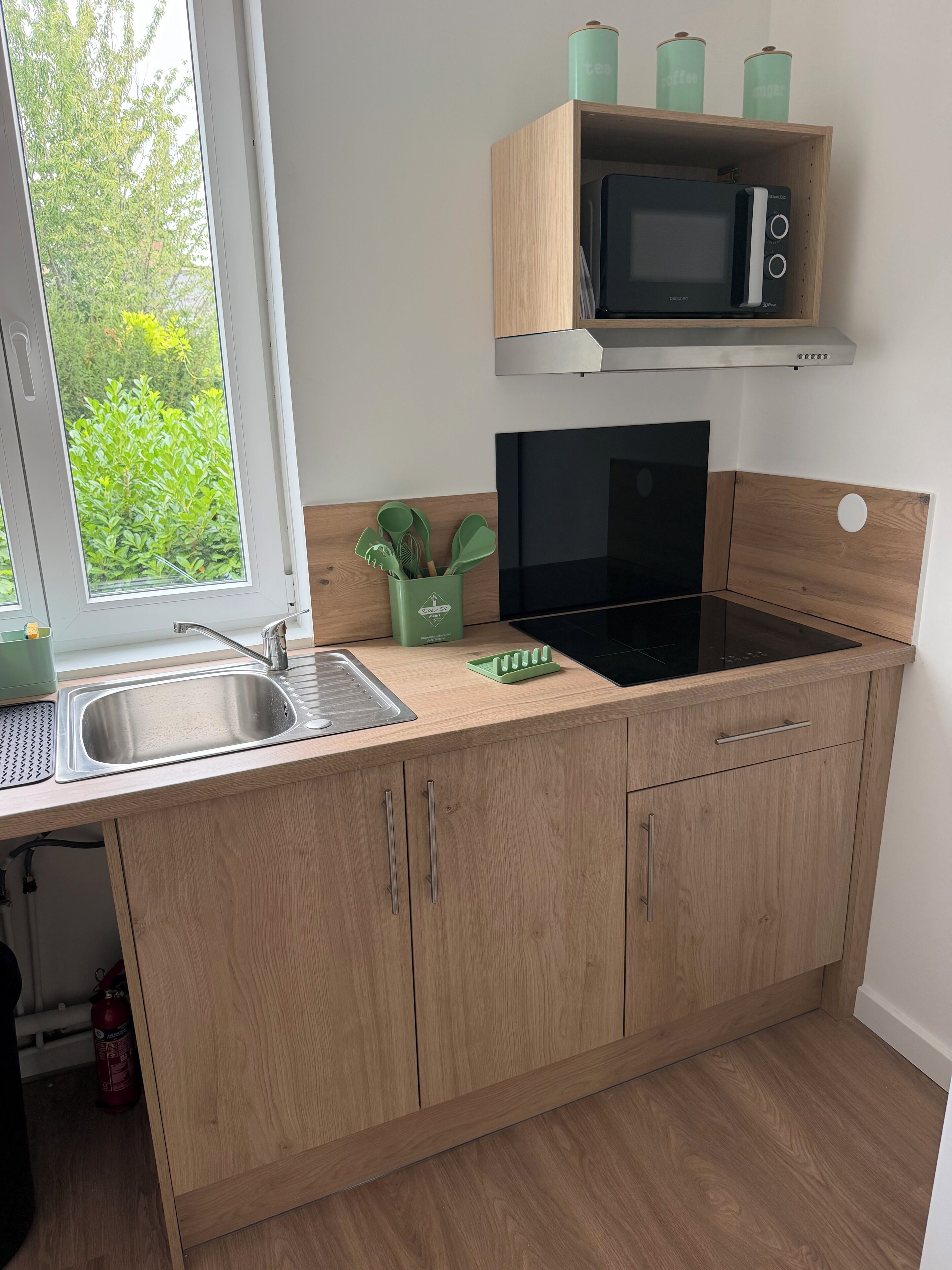 Una cocina con un lavamanos de acero inoxidable, un microondas, una placa de inducción y armarios de madera.