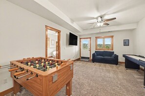 Ein Zimmer mit Tischfußball, einer Couch, einem Deckenventilator und einem Fenster mit Blick.