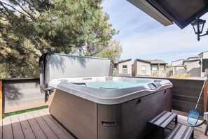 Un jacuzzi en una terraza de madera con vistas a casas al fondo.