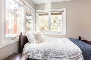 A bedroom with a bed, a nightstand, and a window with a view of buildings and trees. - Spacious 5-bedroom condo, base of Big Cottonwood Canyon in Cottonwood Heights (Cottonwood Heights)