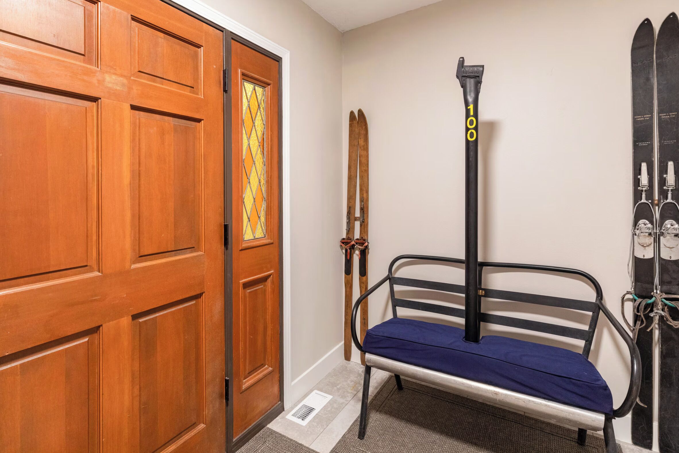 A room with a wooden door, a bench, skis, and a ski lift pole.