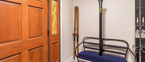 Una habitación con puerta de madera, un banco, esquíes y un poste de telesilla.