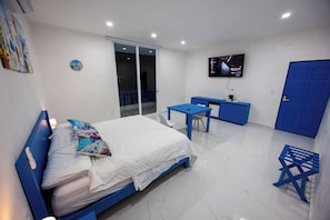 A room with a bed, a desk, a chair, a TV, and a door. - Have you heard of Santorini? Come experience Santorini in Greece. Themed Hotel (Mérida)