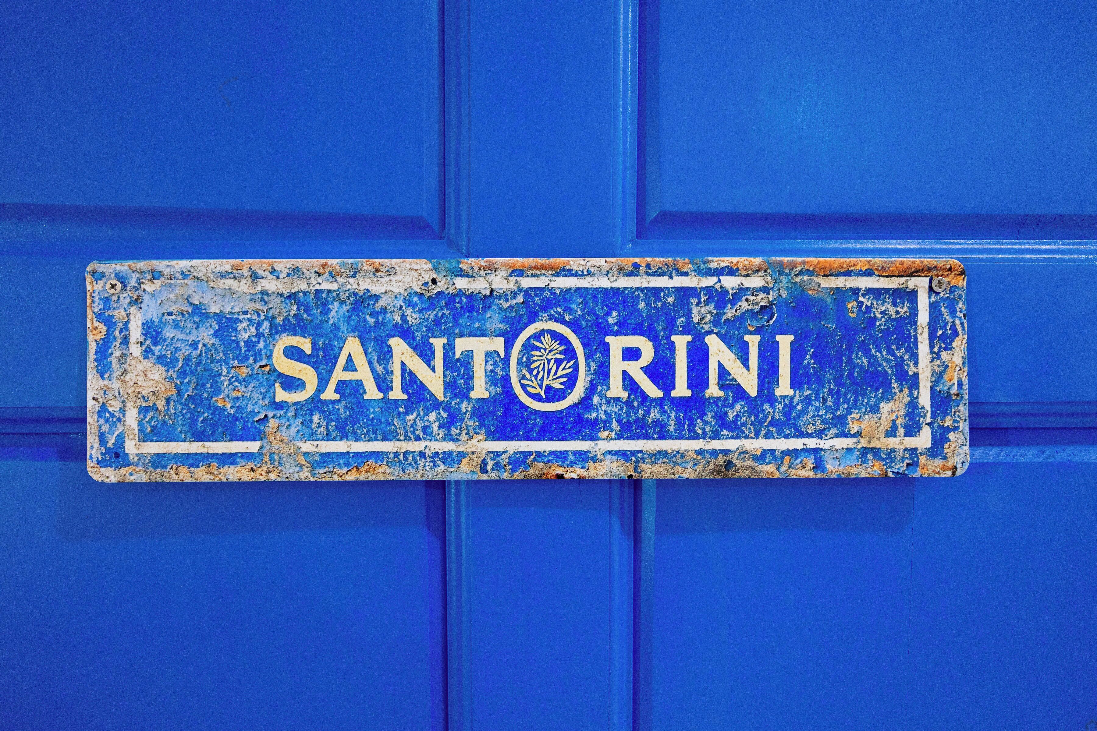 Une porte bleue ornée d’une enseigne usée sur laquelle on peut lire « SANTORINI ».