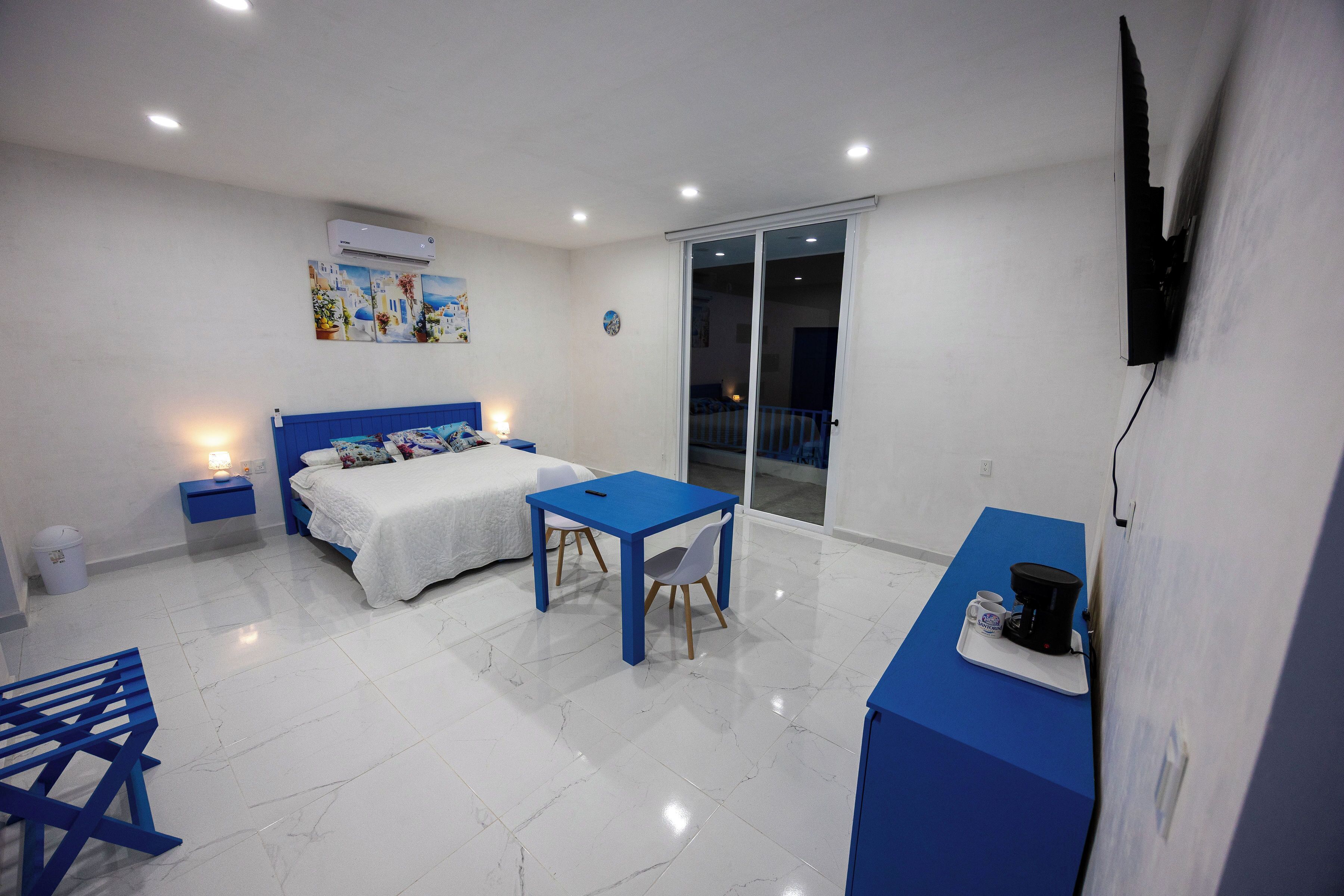 A hotel room with a bed, a desk, a chair, a coffee maker, and a TV.