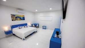 A hotel room with a bed, a desk, a chair, a painting, and a television. - Have you heard of Santorini? Come experience Santorini in Greece. Themed Hotel (Mérida)