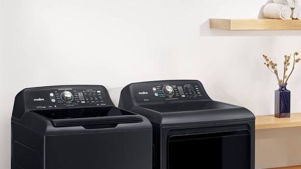 Two black front-loading washing machines with control panels, placed next to a wooden shelf with a vase of dried flowers. - Have you heard of Santorini? Come experience Santorini in Greece. Themed Hotel (Mérida)