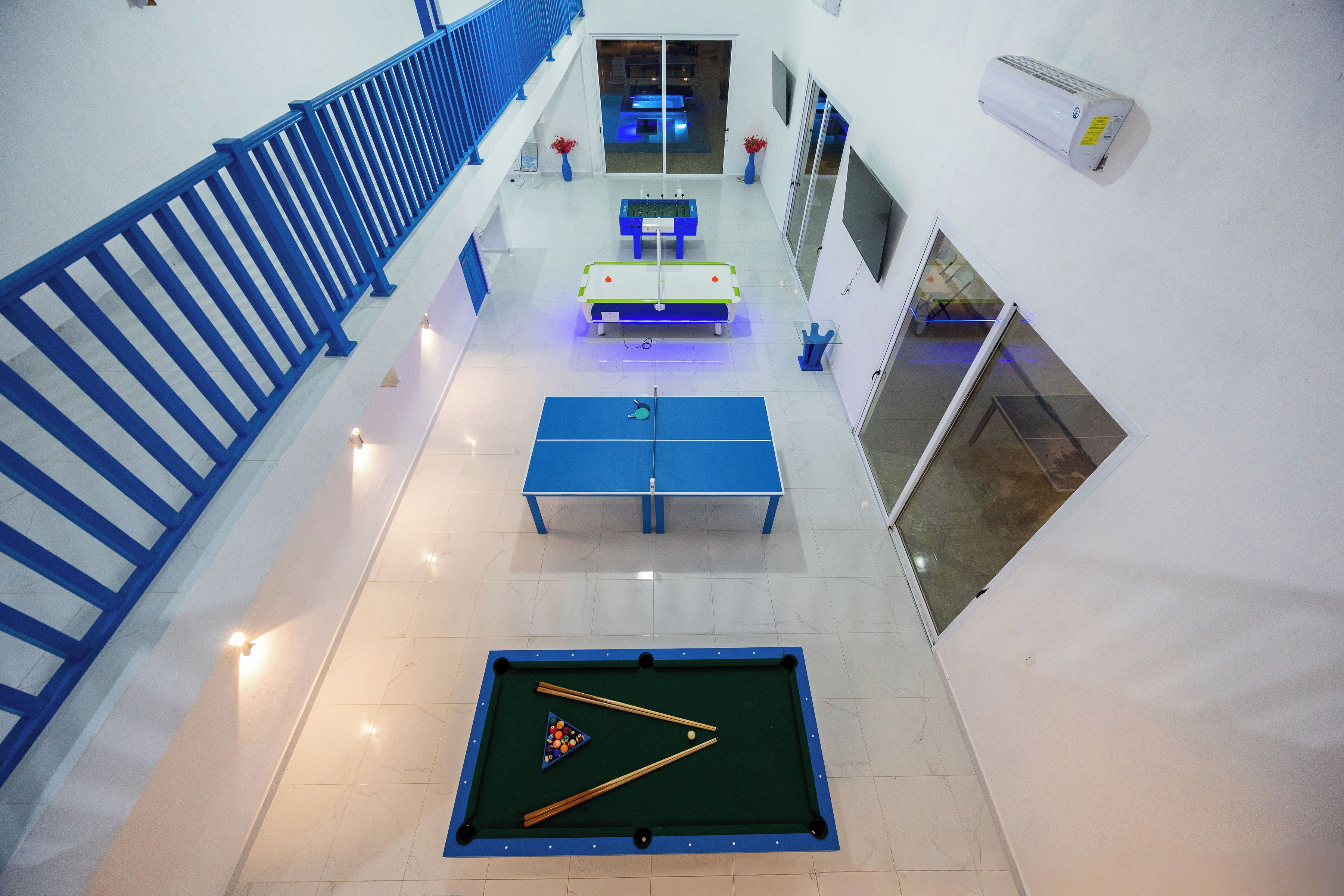 Un espace de loisirs intérieur à plusieurs niveaux, comprenant une table de billard, une table de ping-pong et une table de jeu de fléchettes.