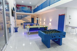 A spacious indoor area with two foosball tables, a billiards table, and a staircase leading to an upper level. - Have you heard of Santorini? Experience Santorini in Greece. Themed Hotel (Mérida)