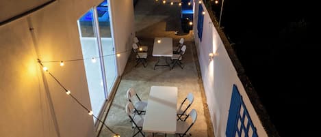 An outdoor seating area with tables and chairs, string lights, and a blue wall.