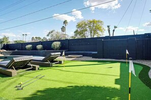 Ein gepflegter Rasen mit Putting Green, Liegestühlen und einem Golfwagen.