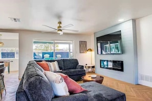 A modern living room with a dark grey sofa, a round coffee table, and a ceiling fan. - Scottsdale Hangout | Pool + Putting Green + Games (Scottsdale)
