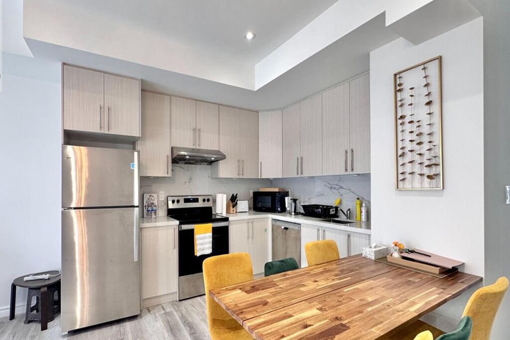 Una cocina moderna con electrodomésticos de acero inoxidable, una mesa de comedor de madera y armarios de colores claros.