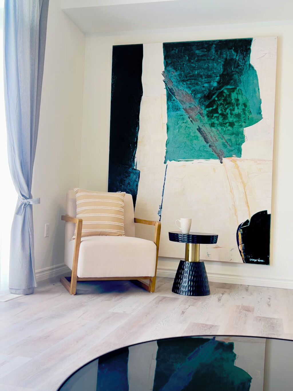 Een moderne kamer met een witte fauteuil, een klein rond tafeltje met een witte kop, en abstracte kunst aan de muur.