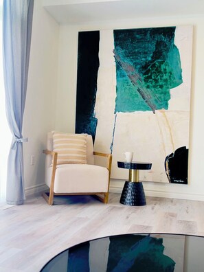 Een moderne kamer met een witte fauteuil, een klein rond tafeltje met een witte kop, en abstracte kunst aan de muur.