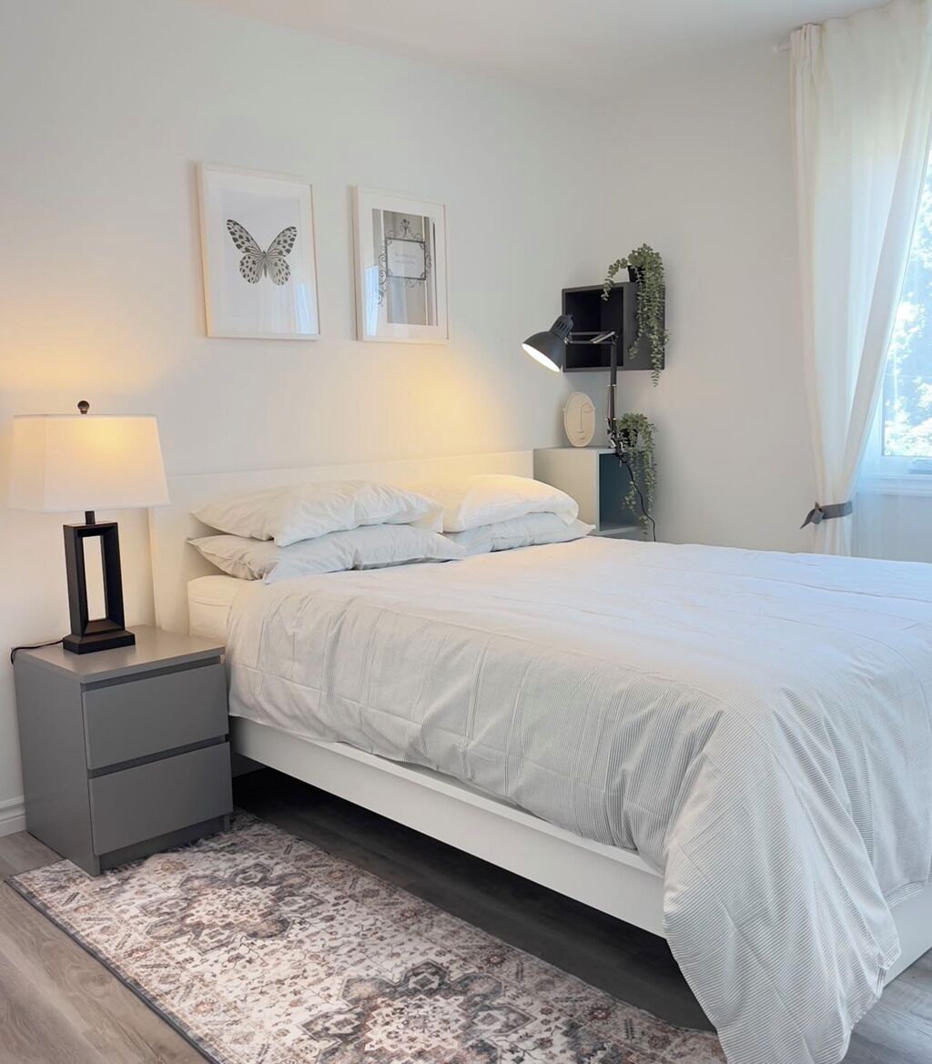A bedroom with a bed, nightstands, a lamp, wall art, and a window with curtains.