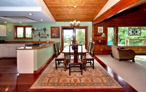A spacious kitchen with a central island, wooden dining table with chairs, and a large window overlooking greenery. - Very unique 3-bedroom house on wooded lot near town with great view and privacy. (Homer)