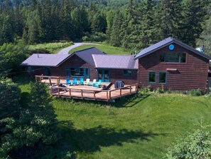 A cabin with a deck and outdoor seating area, surrounded by a forested landscape. - Very unique 3-bedroom house on wooded lot near town with great view and privacy. (Homer)