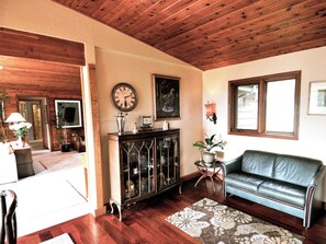 A living room with a wooden ceiling, a sofa, a cabinet with glass doors, and a clock on the wall. - Very unique 3-bedroom house on wooded lot near town with great view and privacy. (Homer)