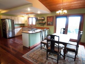 A kitchen with a central island, dining table with chairs, wooden cabinets, and a chandelier. - Very unique 3-bedroom house on wooded lot near town with great view and privacy. (Homer)