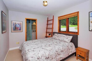 Un dormitorio con cama, mesita de noche, escalera, ventana y puerta.